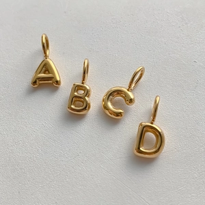 Close-up of 14K gold plated bubble letter A B C D pendants with polished finish