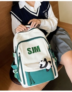 Detail of canvas school backpack with green SJM letters and cute panda plush pendant