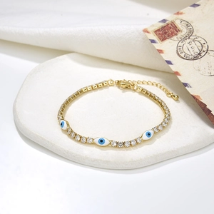Detail of gold-plated bracelet with blue evil eye charms and claw-set zircon stones