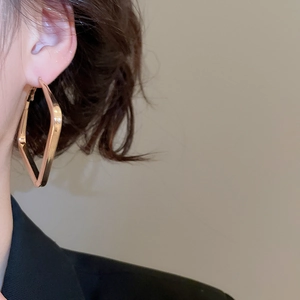 Macro side view of a model wearing large geometric rhombus gold hoop earrings
