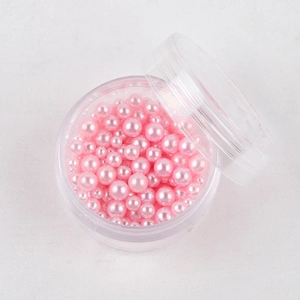 Perle rotonde iridescenti rosa in varie dimensioni in una scatola di plastica trasparente