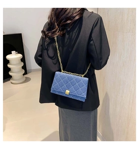 Detail view of a blue quilted denim crossbody bag with a gold chain strap on a model