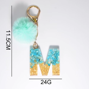 Detail of blue resin letter M keychain with mint pompom and golden stone glitters