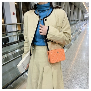 Close-up of orange PVC quilted crossbody bag with golden chain strap on a model