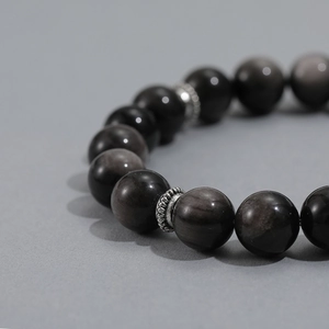 Macro detail of obsidian beaded bracelet with vintage silver charms and natural metallic luster