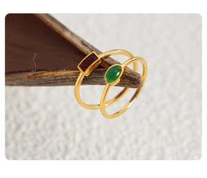 Detail of slim gold rings featuring emerald green and ruby red gemstones on a wooden branch