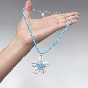 Detail of light blue beaded necklace with white shell flower pendant and gold extension chain
