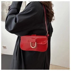 Side view of red patent leather handbag with gold horsebit buckle on a trench coat