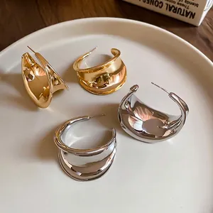 Set of thick gold and silver chunky C-shaped hoop earrings on a ceramic display plate