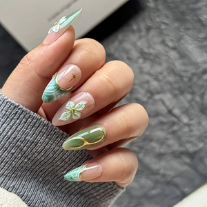 Detail of almond-shaped emerald green press-on nails with 3D white flowers and gold stars