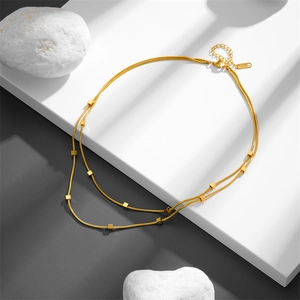 Golden double-layer snake chain necklace with cubes on a minimalist geometric white stand