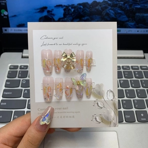 Detail of handmade press-on nails featuring pink gradient, metal bows and butterfly charms