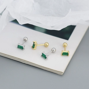 Macro shot of silver and gold stud earrings with emerald-cut green zircons on a white card