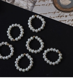 Detail of six elastic freshwater pearl rings with 14K gold-filled beads on black background