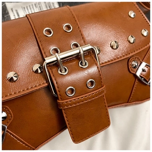 Detail of brown punk style shoulder bag featuring silver metal rivets and a large buckle