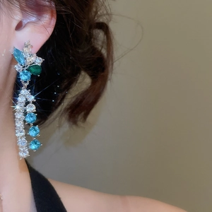 Detail of silver floral drop earring with sparkling blue and green crystals on model