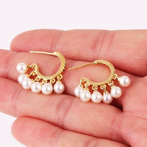 Detail of hand holding gold hoop earrings with five hanging pearls in a vintage style