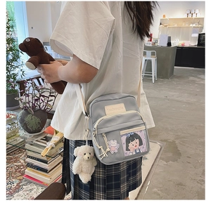 Détail du sac à bandoulière en nylon bleu clair avec breloque ours et écussons