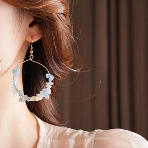 Close-up of gold hoop earrings with light blue and white natural stones on a model