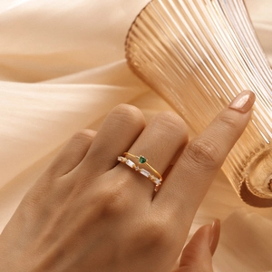 Close-up of double-layered gold rings with green heart stone and white baguette zircons