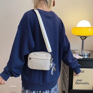 Model view of beige crossbody bag with adjustable strap in a lifestyle home setting
