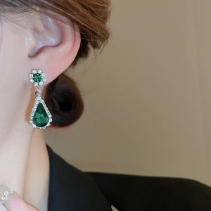 Detailed view of luxury green water drop earrings with clear diamonds on model's ear