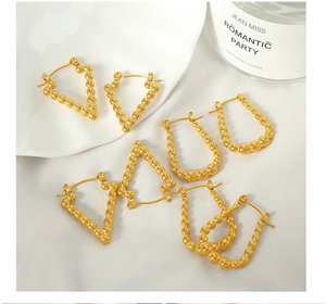 Close-up of geometric gold bead earrings with triangle and oval shapes on a white tray
