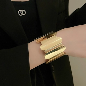 Close-up of wide polished gold cuff bracelet featuring elegant scalloped edges on wrist