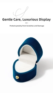 Detailed view of luxury navy blue heart-shaped velvet ring box with gold button and white lining