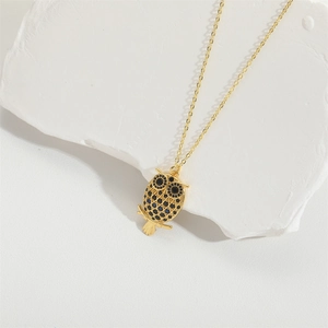Elegant gold owl pendant necklace with black and blue rhinestones on white stone