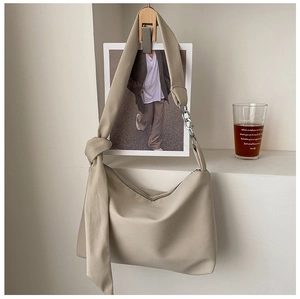Detail of a minimalist beige crossbody bag featuring a metal chain and wide fabric strap