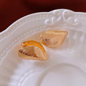 Minimalist vintage shell-shaped golden earrings with textured metal finish on white plate