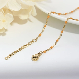 Macro detail of gold lobster clasp and orange enamel beads on stainless steel chain