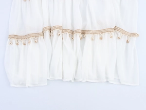 Detail of white bohemian fabric with khaki woven trim and hanging bead tassels