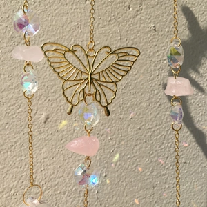 Detailed view of golden butterfly pendant with pink crystal beads and hanging metal chains