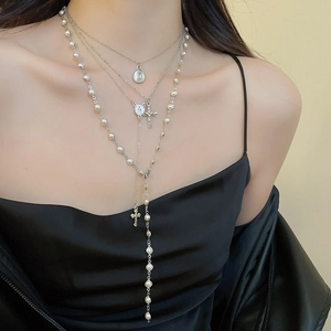 Detail of layered Y2K cross and pearl necklace set worn on neck with silver pendants