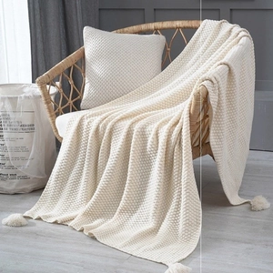 Close-up of cream waffle knit throw blanket with decorative tassels on a rattan chair