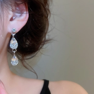 Close-up of elegant silver teardrop earrings with crystal stones worn by a model