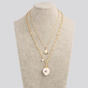 Detail of layered gold-tone necklace with white spiral conch shell and round pearl charms