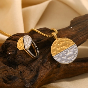 Detail of two-tone gold and silver textured ring and necklace set on a dark wood surface