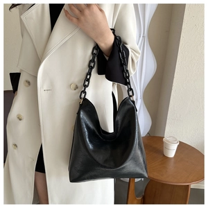 Detail of glossy black shoulder bag with chunky chain strap on a model in interior