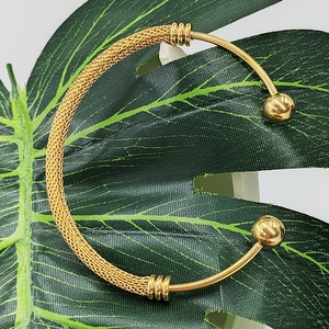 Macro view of gold mesh weave open bangle with smooth bars on green leaf background