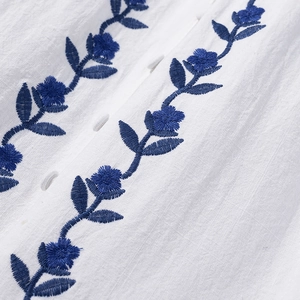 Detailed macro view of white fabric with blue floral embroidery and white buttons