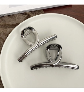 Close-up of two minimalist silver metal hair claws with a modern twisted geometric design