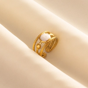 Golden woven rope ring with white circular inlay on soft beige fabric background