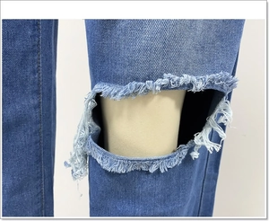 Macro-opname van de gescheurde knie en gerafelde details van de blauwe high waist jeans