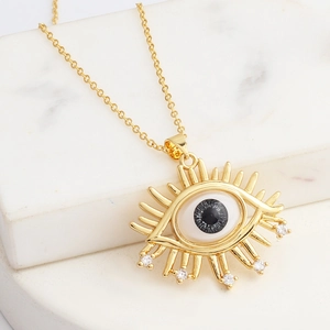 Detail eines goldenen Evil Eye Anhängers mit weißem Muscheleinleger und Kristallen
