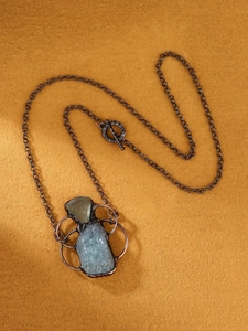 Macro detail of handmade aquamarine and fluorite raw stone pendant on a bronze chain