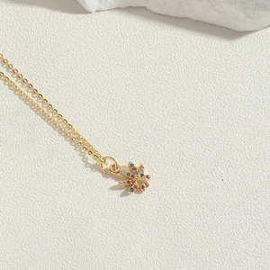 Macro detail of gold maple leaf pendant with colorful zircon stones on thin chain