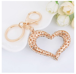 Close-up of golden hollow heart keychain with sparkling crystals on white rose background